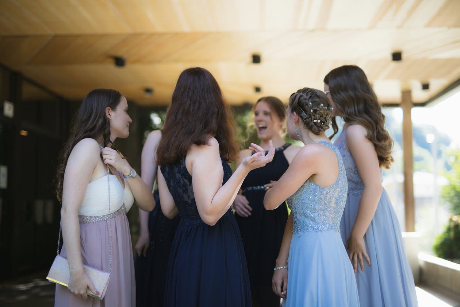 Gruppe von Frauen in eleganten Abendkleidern bei einer Unterhaltung draußen im Sonnenlicht.